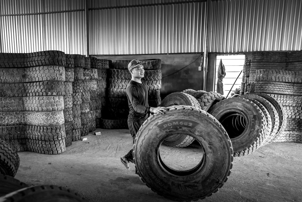 hero-img-01 Man in black and white monochrome scene with stacked tires in industrial setting.