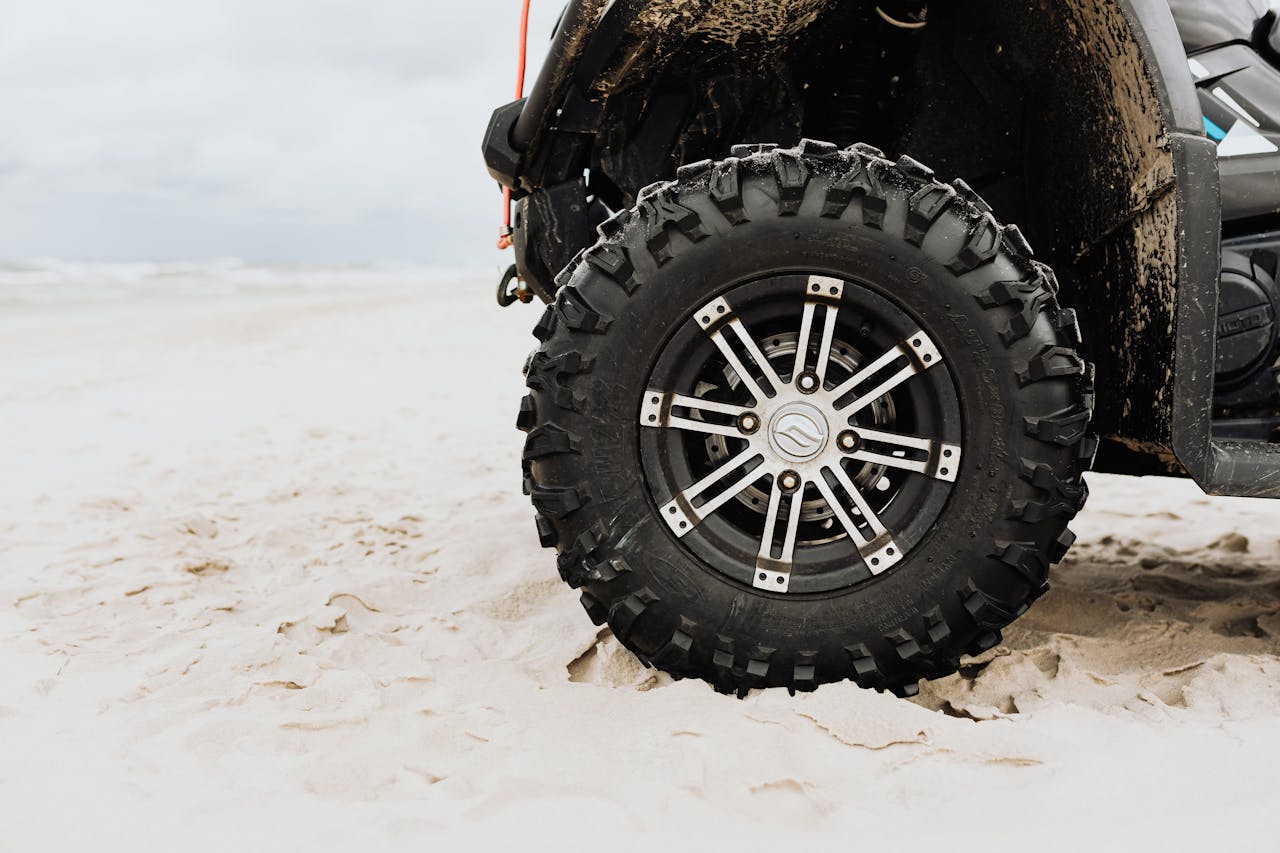 gallery-5 Close-up of an all-terrain vehicle tire on a sandy beach, showcasing rugged design and off-road capabilities.