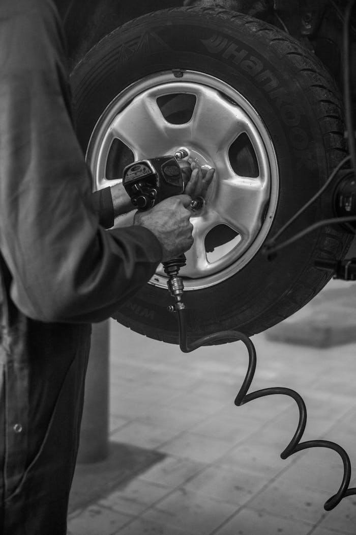 gallery-2 Mechanic uses air wrench to fix car tire in a monochrome garage setting.