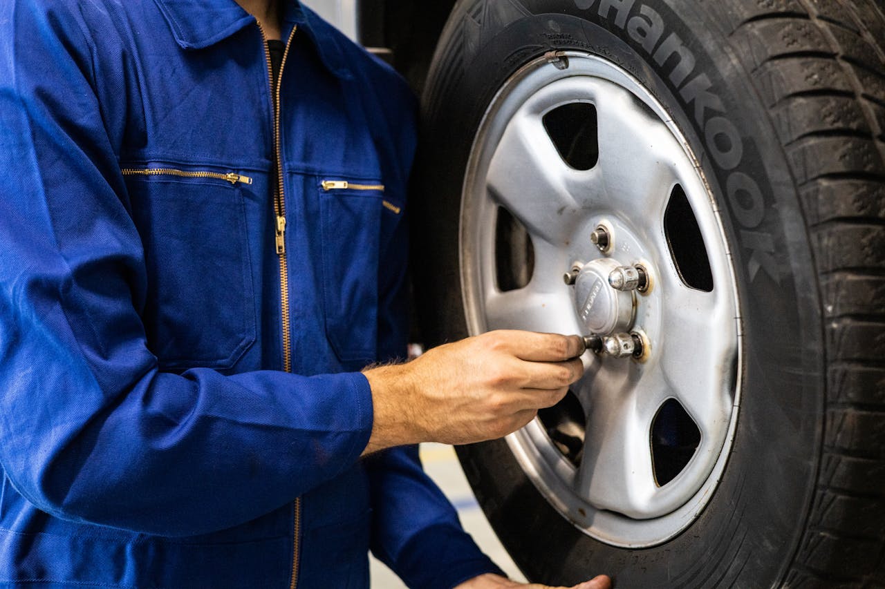 gallery-1 Mechanic in blue coveralls inspecting a car tire in an auto repair workshop.